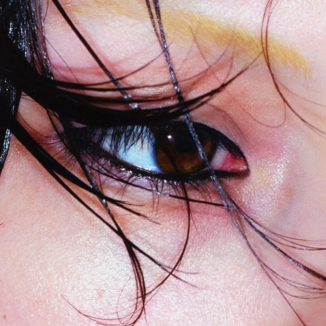 Close-up shot of a woman's brown eye with black eyeliner, eyelashes, and wet strands of black hair on her face. Beauty shot.