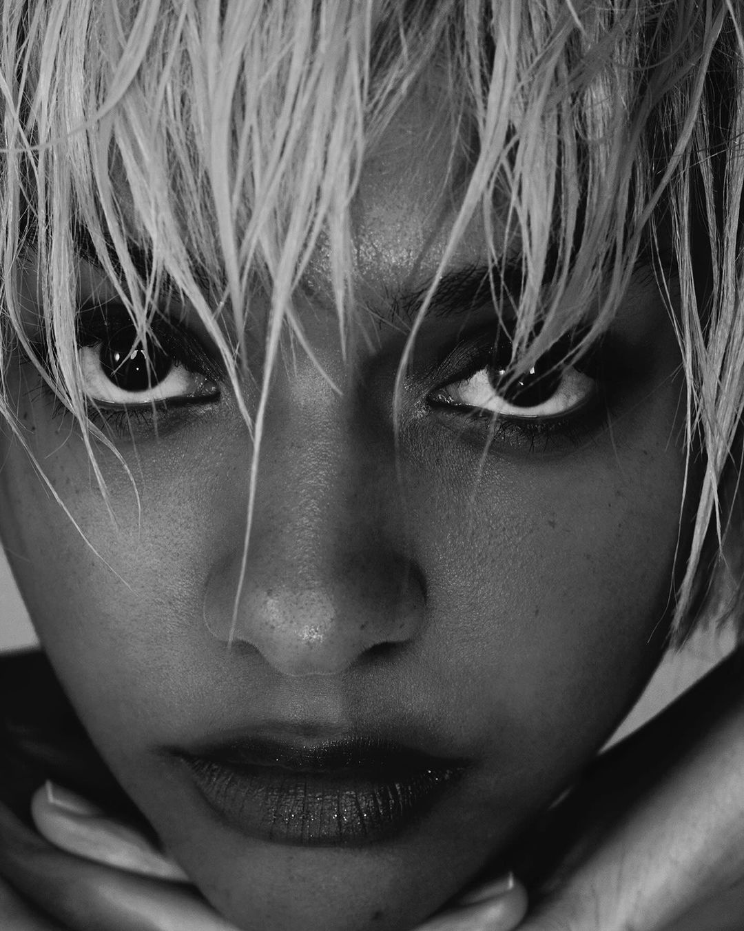 Close-up black and white portrait of an adult female with wet, short white hair, dark eyes, and neutral facial expression.