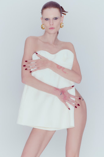 Artistic portrait of a slender woman with red hair and bold makeup posing with a white towel in a photo studio setting.