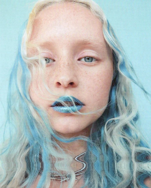 Close-up of a young adult female with white-blonde hair and light blue highlights, wearing sparkling blue lipstick and a silver necklace.