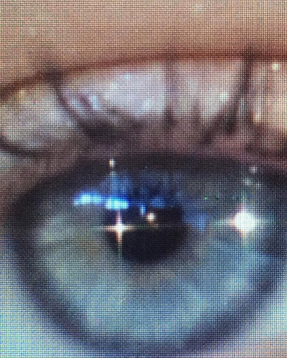 Close-up shot of a blue human eye with visible eyelashes and skin texture surrounding the eye area, featuring light reflections.