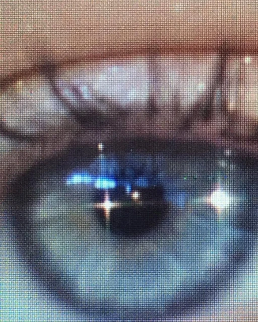 Close-up shot of a blue human eye with visible eyelashes and skin texture surrounding the eye area, featuring light reflections.