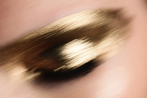 Close-up of blurred gold makeup smear on light pink skin; beauty and cosmetic concept with motion blur and a soft, diffused focus.