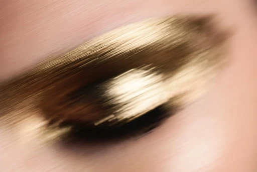 Close-up of blurred gold makeup smear on light pink skin; beauty and cosmetic concept with motion blur and a soft, diffused focus.
