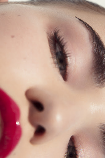 Close-up portrait of a woman with glossy red lips and detailed eye makeup, emphasizing beauty and cosmetic details.