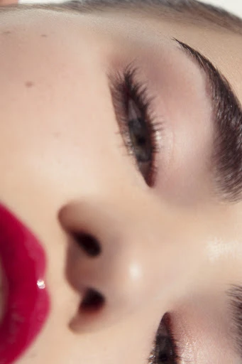 Close-up portrait of a woman with glossy red lips and detailed eye makeup, emphasizing beauty and cosmetic details.