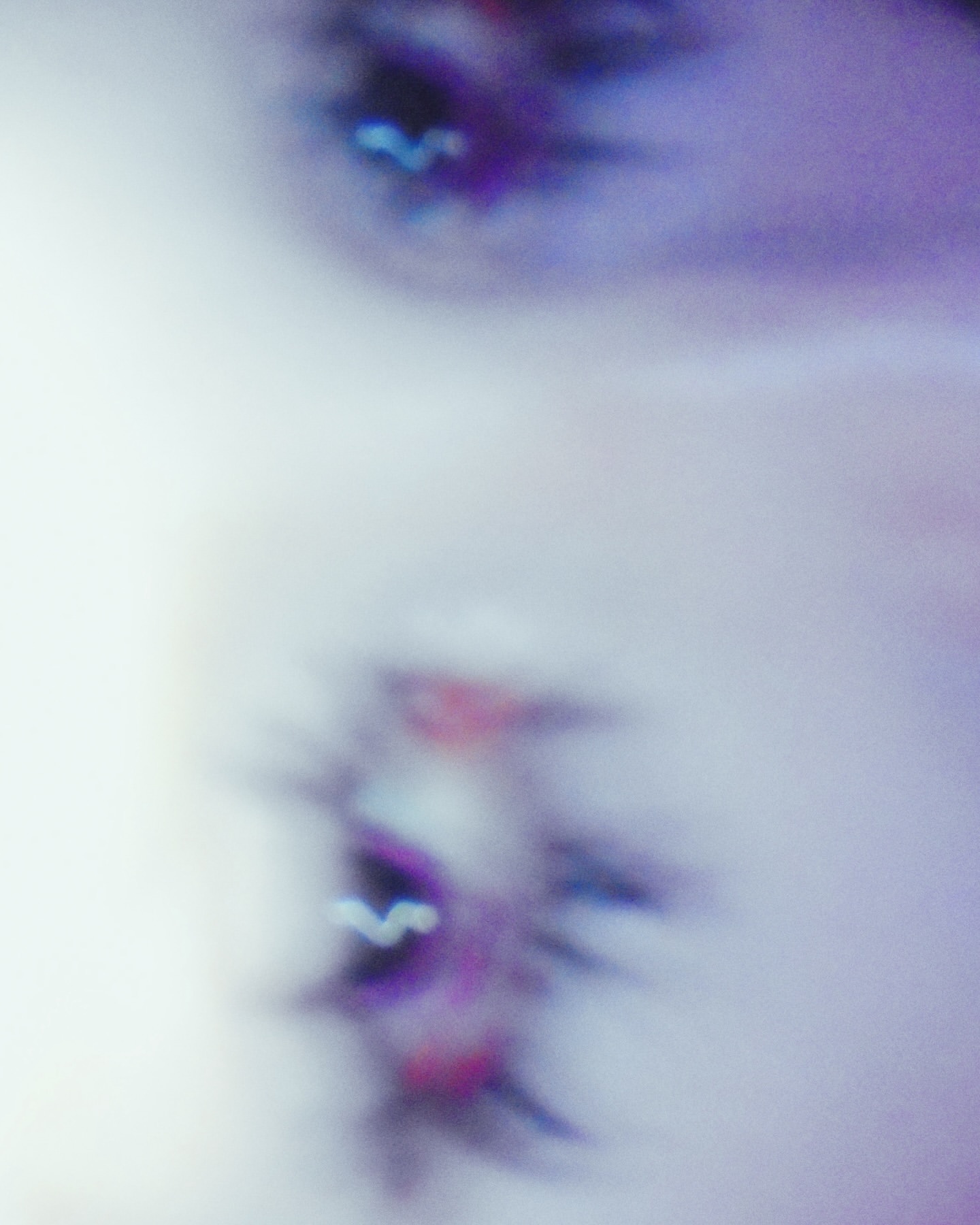 Close-up of a fair-skinned person's face with open mouth, showing teeth and the blurred view of an eye in a blurred, light-filled scene.