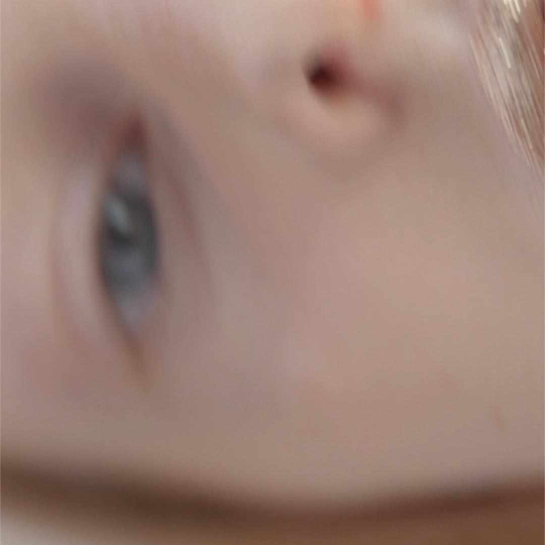 Extreme close-up of a baby's face, highlighting the pale skin, nose, and one blue eye, with a blurred background, creating a soft, intimate feel.