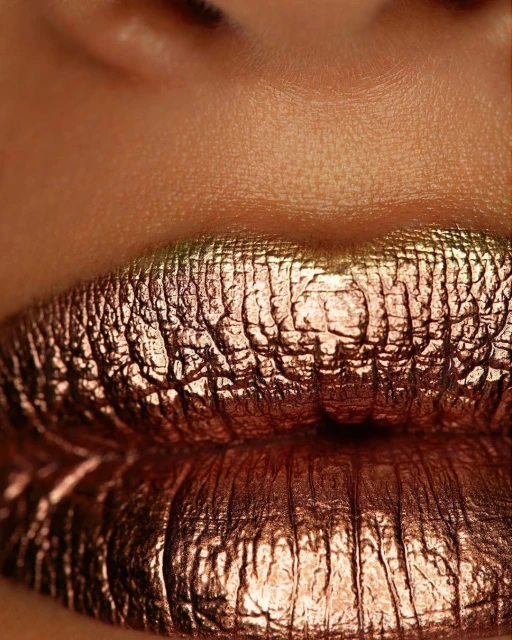 Close-up of a woman's face featuring metallic copper lipstick with a textured, foil-like appearance, accentuating the lips.