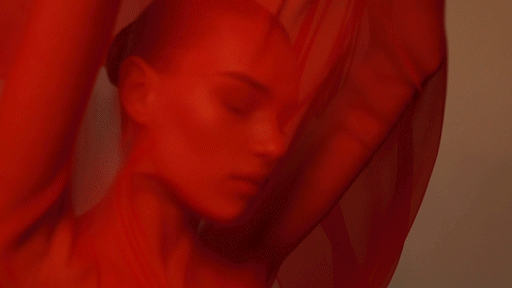 Woman with eyes closed posing with a red flowing fabric, bathed in red light. Ethereal beauty fashion shot, minimal background.
