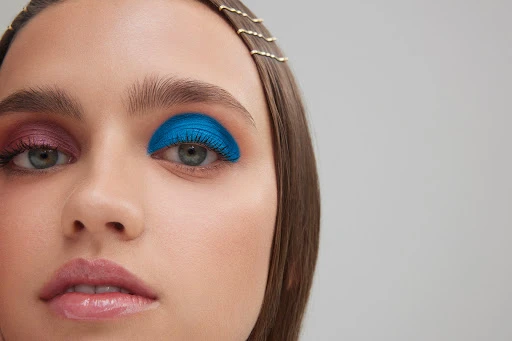 Close-up of a woman's face, showcasing dramatic, colorful eye makeup with one eye in blue and the other in pink eyeshadow.