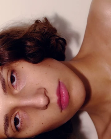 Close-up portrait of a woman with brown hair and pink lipstick shot by Anairam against a plain background