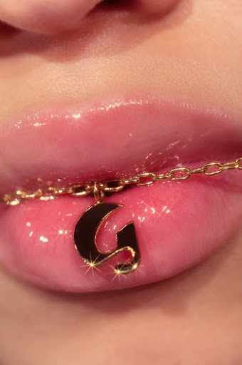 Close-up of glossy lips with a gold initial pendant necklace featuring the letter G, beauty shot for fashion and personal expression.