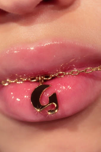 Close-up of glossy lips with a gold initial pendant necklace featuring the letter G, beauty shot for fashion and personal expression.