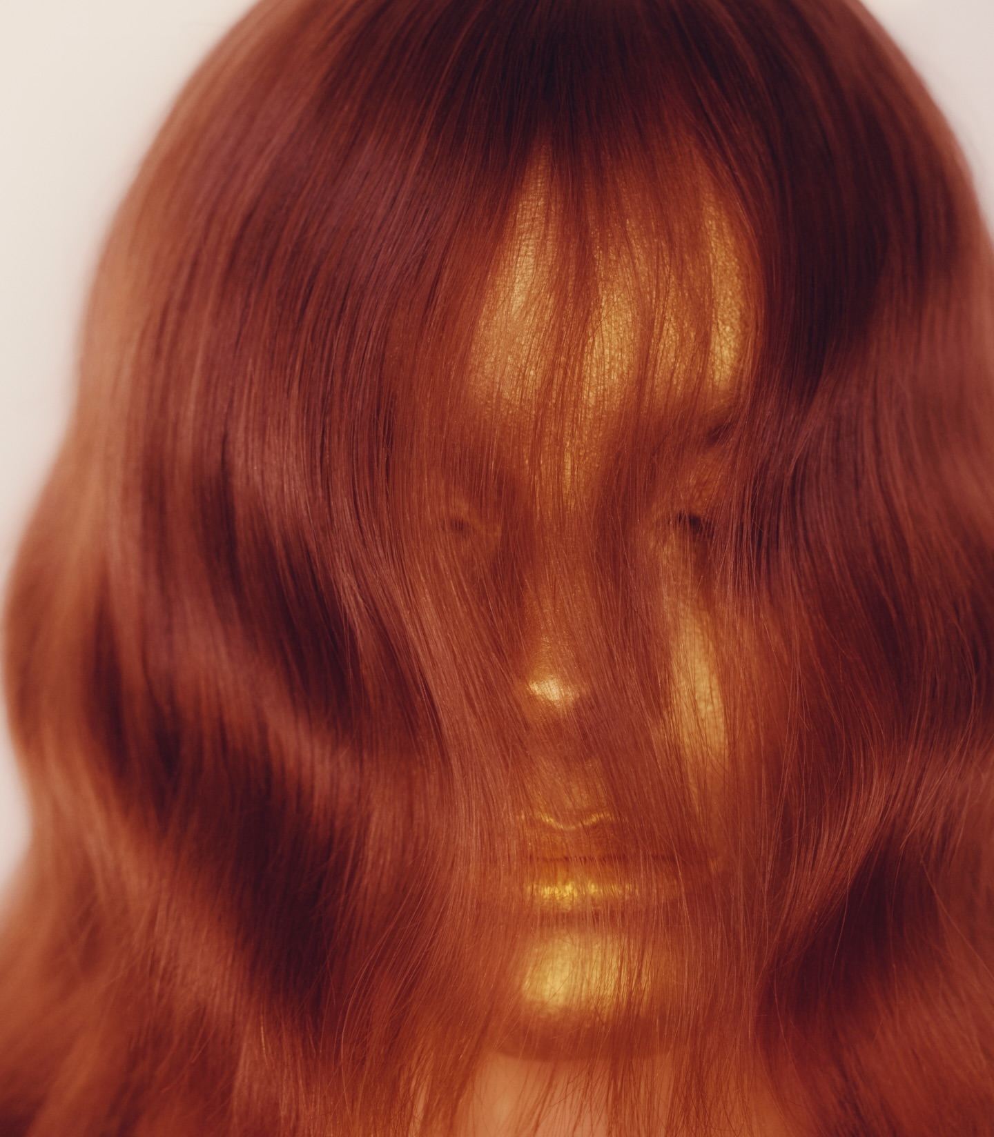 Artistic portrait featuring an adult female with a gold-painted face and copper-red hair obscuring her eyes, creating a textured and surreal aesthetic.