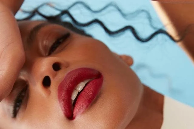 Close-up beauty portrait of a woman with bold red lipstick and dark wavy hair against a light blue backdrop