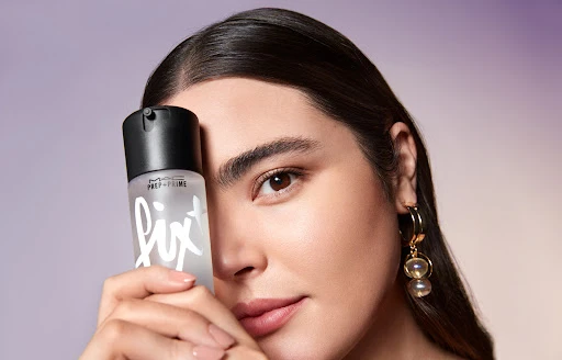 Close-up of a woman holding a MAC Prep+Prime Fix+ bottle, showcasing beauty and cosmetic product promotion with soft lighting.