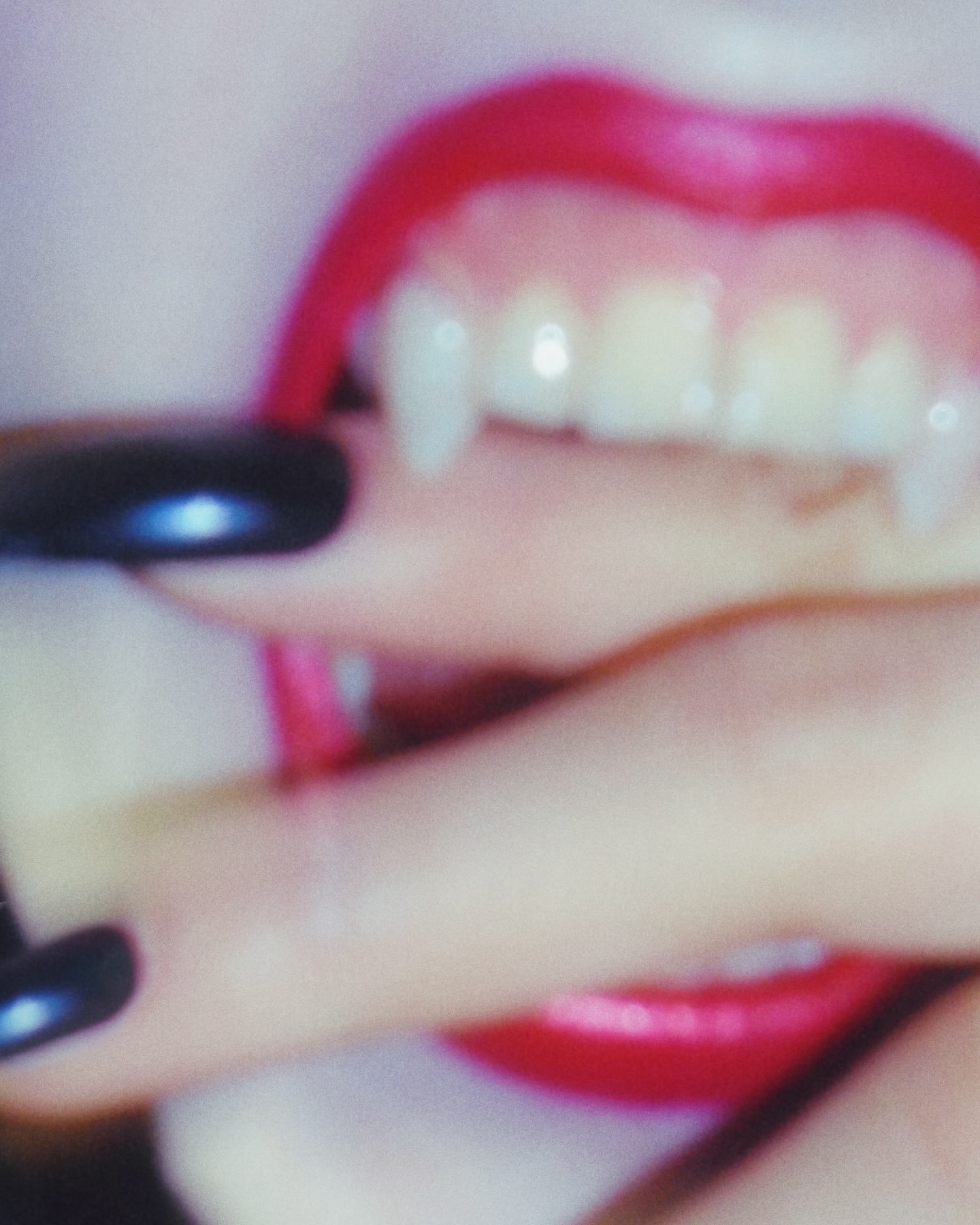 Close-up macro shot of bright red lips showing pointed fangs and fingers with glossy black nails