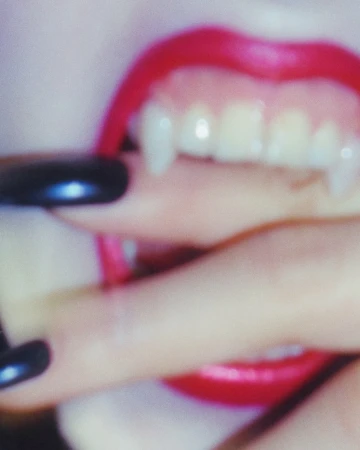 Close-up macro shot of bright red lips showing pointed fangs and fingers with glossy black nails