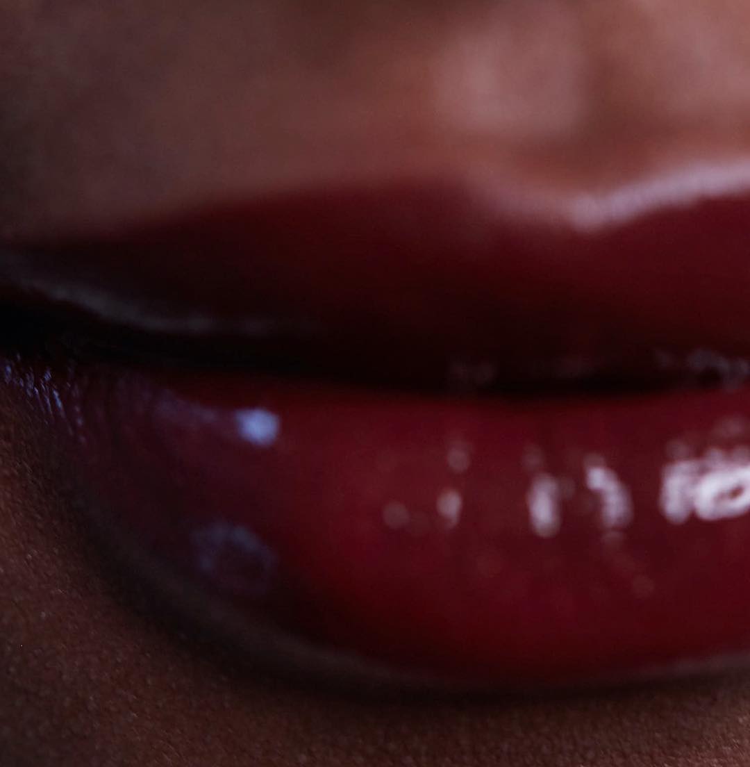 Close-up of an adult female's full lips with a glossy, dark red lipstick. The focus is on the texture and color of the cosmetic.
