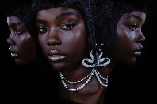 Close-up beauty shot of an adult female with dark skin wearing jewelry against a black background, three images overlapping.