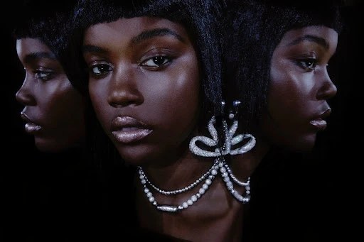 Close-up beauty shot of an adult female with dark skin wearing jewelry against a black background, three images overlapping.