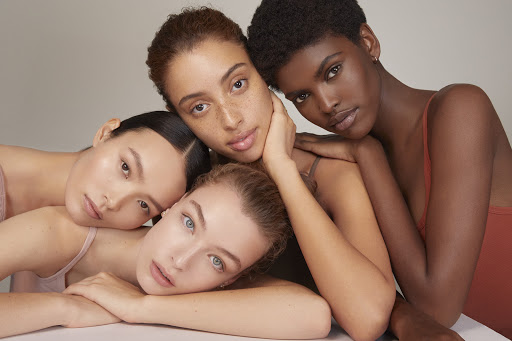 Close-up studio shot of four women with diverse skin tones, huddled together. Beauty, fashion, and skincare concept, neutral background.