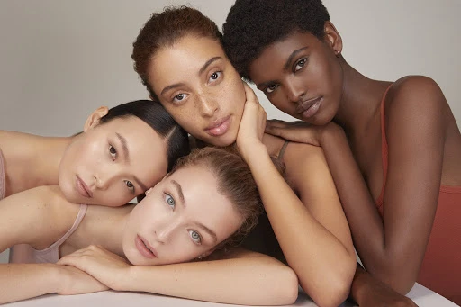 Close-up studio shot of four women with diverse skin tones, huddled together. Beauty, fashion, and skincare concept, neutral background.