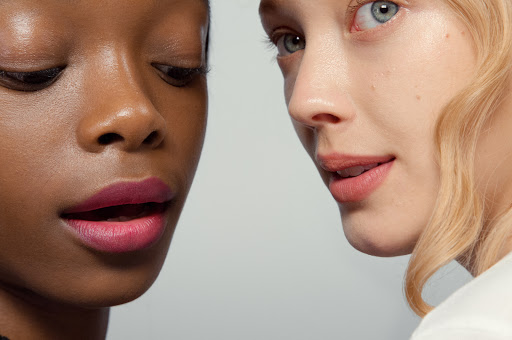 Close-up of two women with fair and dark skin tones wearing vibrant lip color. Beauty shot highlighting diverse skin tones and makeup.