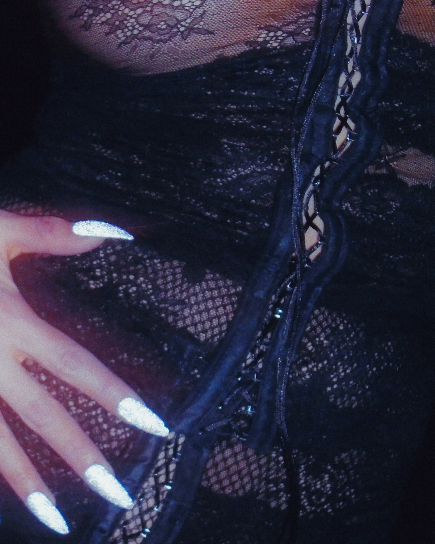 Close-up studio shot of a woman's torso in black lace lingerie and hand with long, silver fingernails, creating a sensual, alluring image.