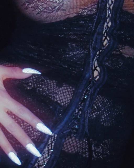 Close-up studio shot of a woman's torso in black lace lingerie and hand with long, silver fingernails, creating a sensual, alluring image.
