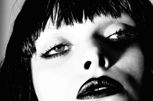 High-contrast black and white close-up portrait of a woman with dark bangs and heavy dark lipstick