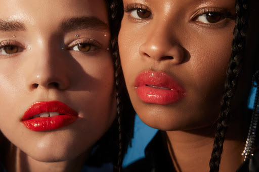 Close-up of two women showcasing red lip gloss. Beauty shot with studio lighting highlighting glossy lips, clear skin, and cosmetic details.