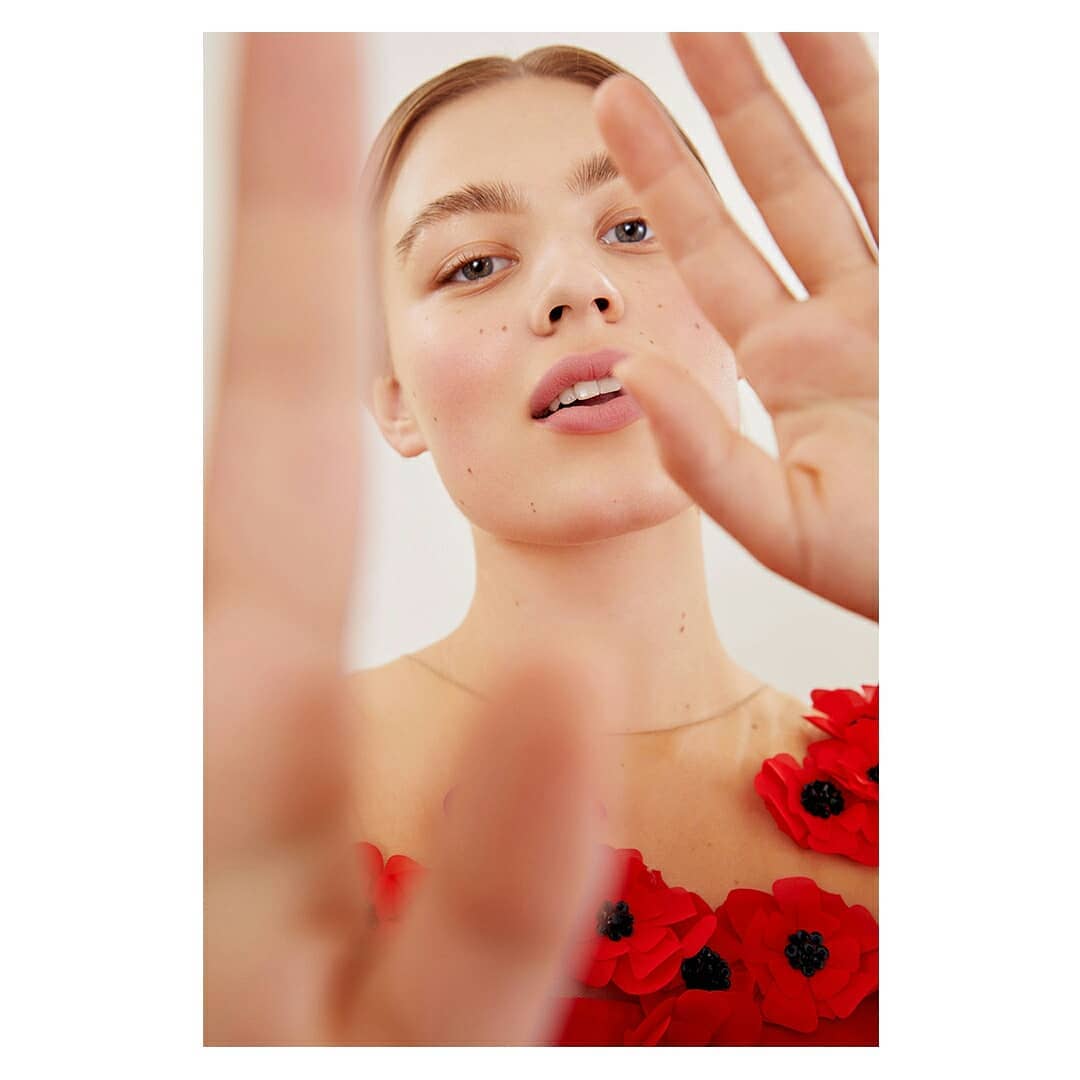 Close-up portrait of a woman with red floral appliqued dress, holding hand up near lens by Anairam