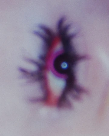 Abstract, blurry image of a stylized eye with black lashes and a pink iris, set against a light purple background with visible grain.