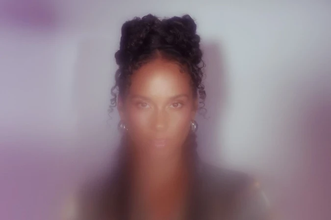 Portrait of a black woman with intricate braided hairstyle and hoop earrings against a soft, hazy background.