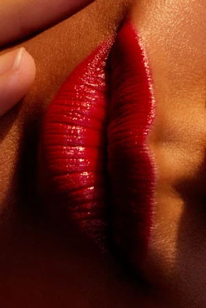 Close-up macro shot of lips wearing glossy red lipstick with a hand touching the face by Anairam.