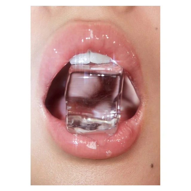 Close-up of a person's mouth with glossy lips and an ice cube held between the teeth, creating a refreshing and eye-catching visual.