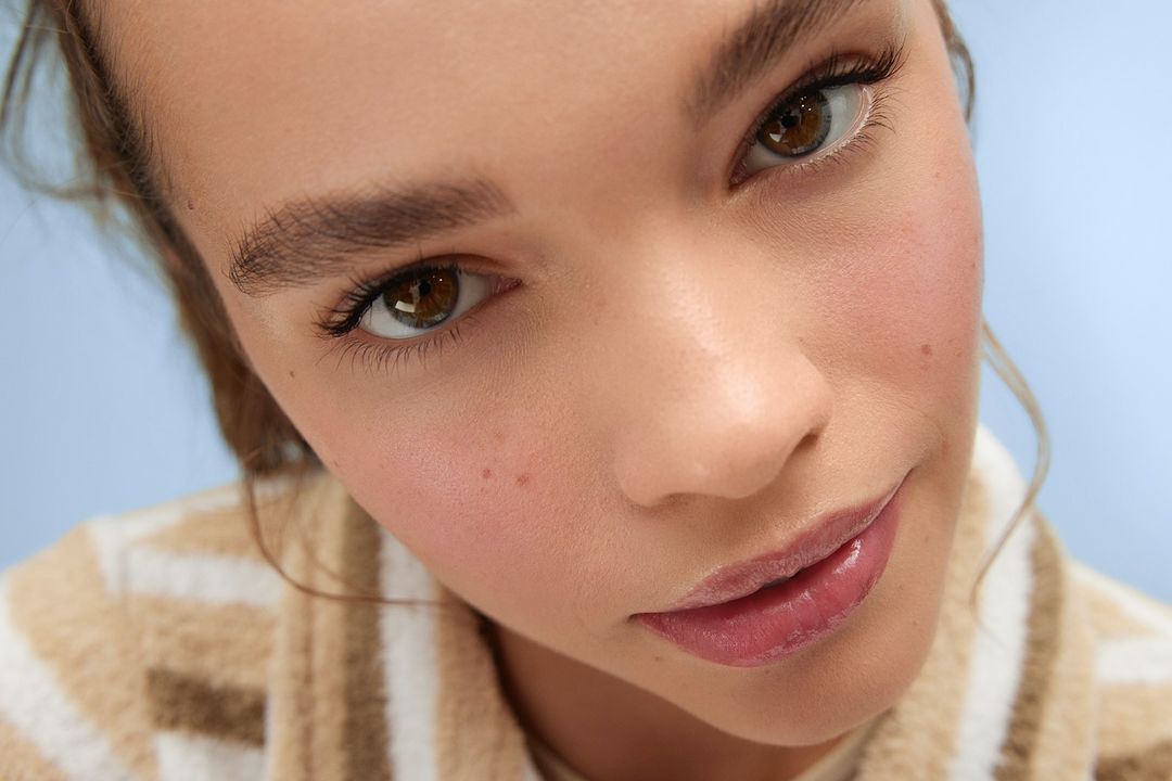 Close-up portrait of a young woman with brown eyes wearing a striped sweater against a pale blue background