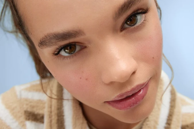 Close-up portrait of a young woman with brown eyes wearing a striped sweater against a pale blue background