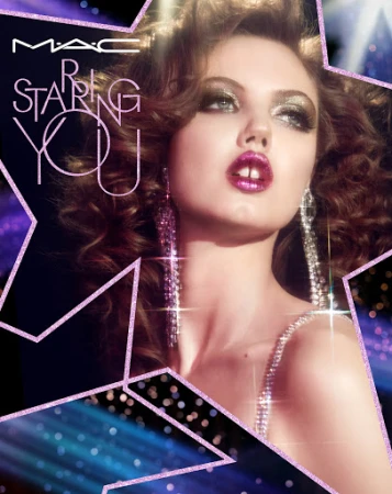 Close-up portrait of a woman with sparkling purple lipstick, voluminous brown hair, and long crystal chandelier earrings.