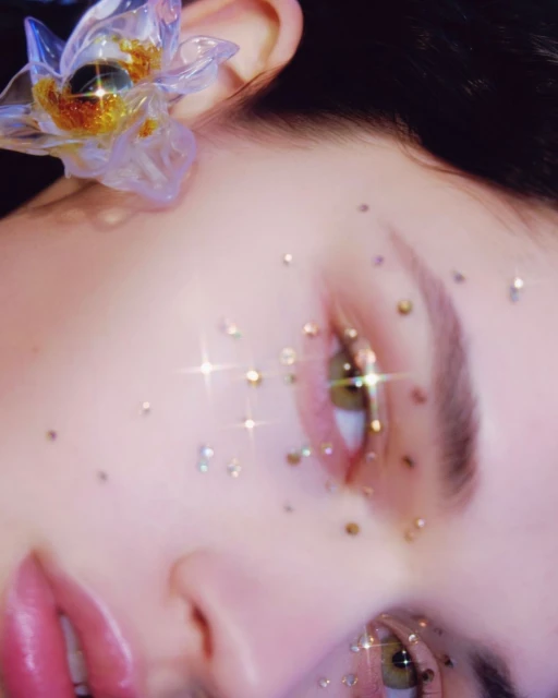 Close-up of a woman's face with sparkly gems around her eyes and a translucent floral hair accessory. Beauty and fashion.