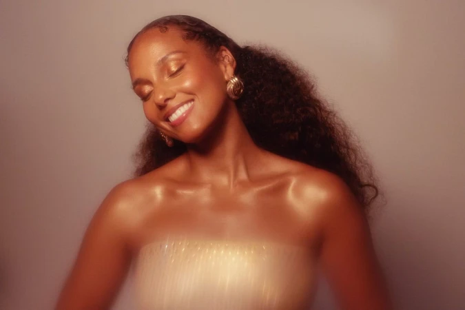 Portrait of a smiling Black woman with dark curly hair and gold earrings against a warm-toned background.