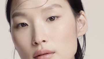 Close-up portrait of an Asian woman with light makeup and slightly wet hair, set against a neutral, monochromatic background.