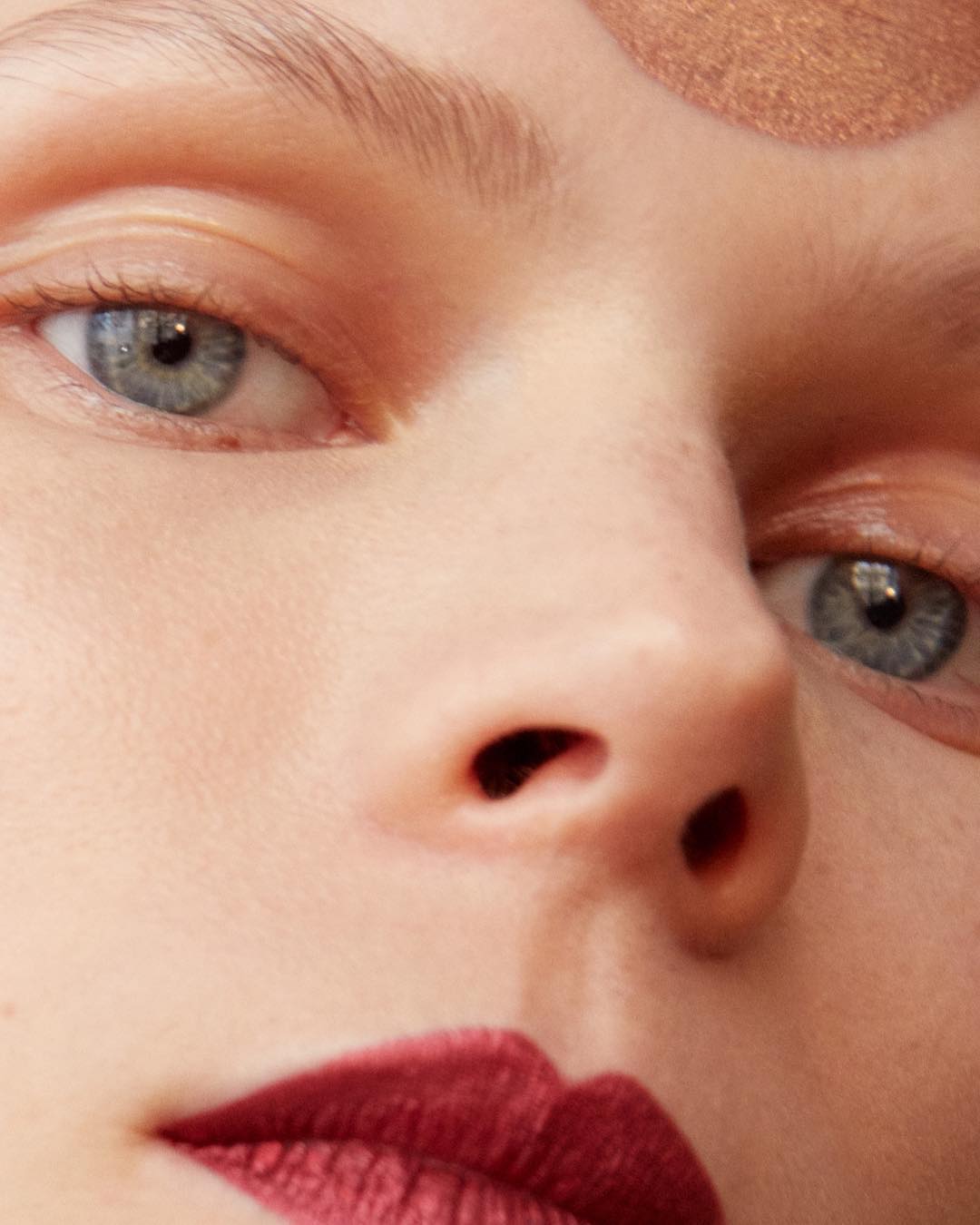 Close-up portrait of a woman's face featuring her blue eyes, nose, and red lips, highlighting the details of her makeup and complexion.