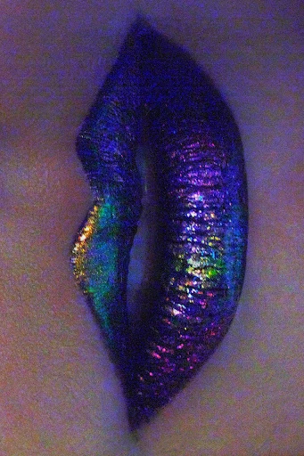 Macro beauty shot of a single human mouth with vivid, iridescent makeup on the lips. The makeup features blue, purple, gold and green colors.