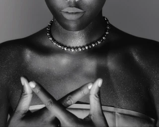 Close-up portrait of a woman wearing a beaded choker necklace with shimmering glitter dust on her skin by Anairam.