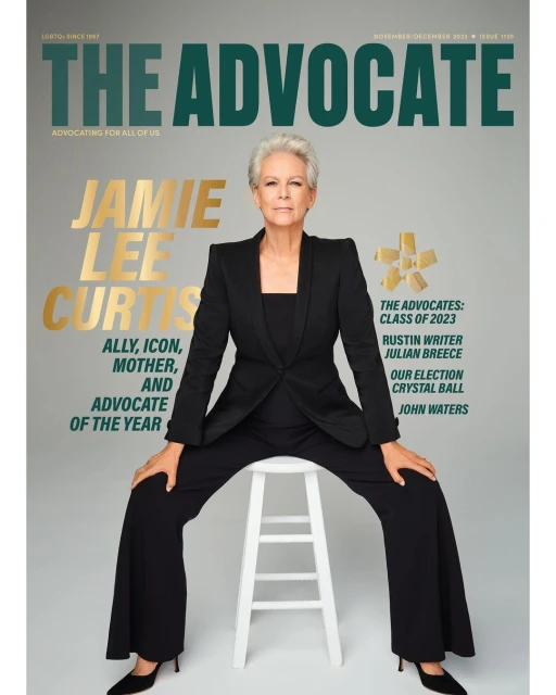 Jamie Lee Curtis on the cover of The Advocate magazine, posed on a white stool, wearing a black suit, with a grey background.