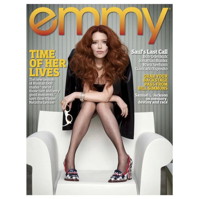 Magazine cover featuring Natasha Lyonne seated in a modern white chair, legs crossed, holding sunglasses, against a striped backdrop.