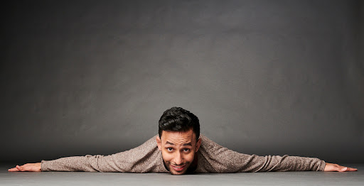 Adult male lying on the floor with his arms outstretched and smiling against a gray background in a photo studio setting.